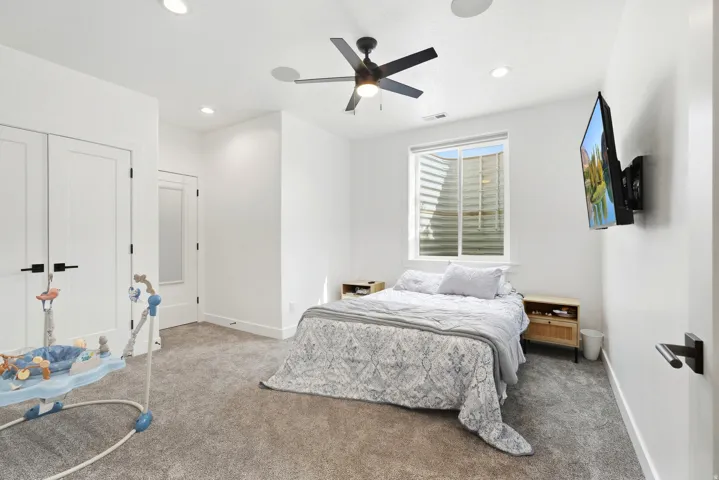 Recessed lighting, ceiling fan, white paneled doors with black hardware, and an egress window