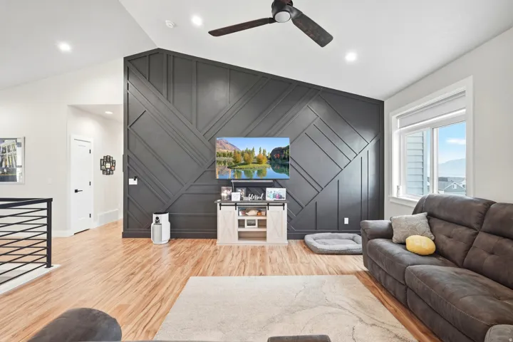 Accent wall with geometric paneling, wood-finish flooring, recessed lighting, ceiling fan, and horizontal wrought iron railing