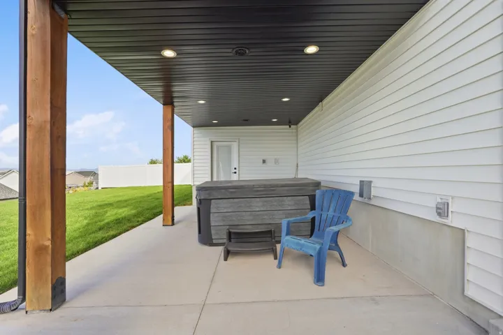 Covered patio with recessed lighting, exposed wood support beams, and a white vinyl privacy fence
