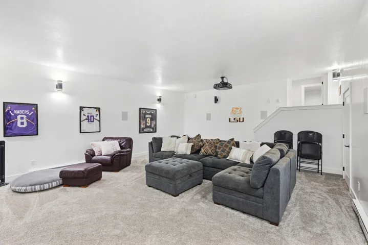 Carpeted living area featuring recessed lighting, wall-mounted light fixtures, a ceiling-mounted projector, and integrated wall speakers