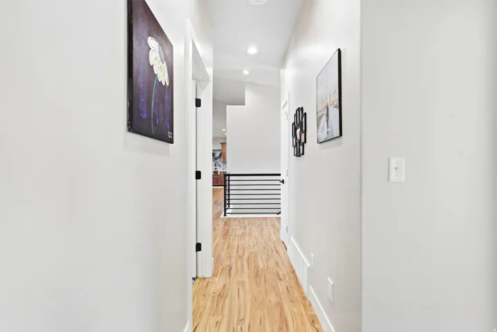 Hallway featuring wood-finish flooring, white walls, recessed lighting, and black metal railings