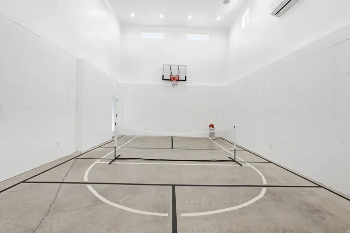 Indoor sports court with concrete flooring, high ceilings, recessed lighting, and a wall-mounted basketball hoop