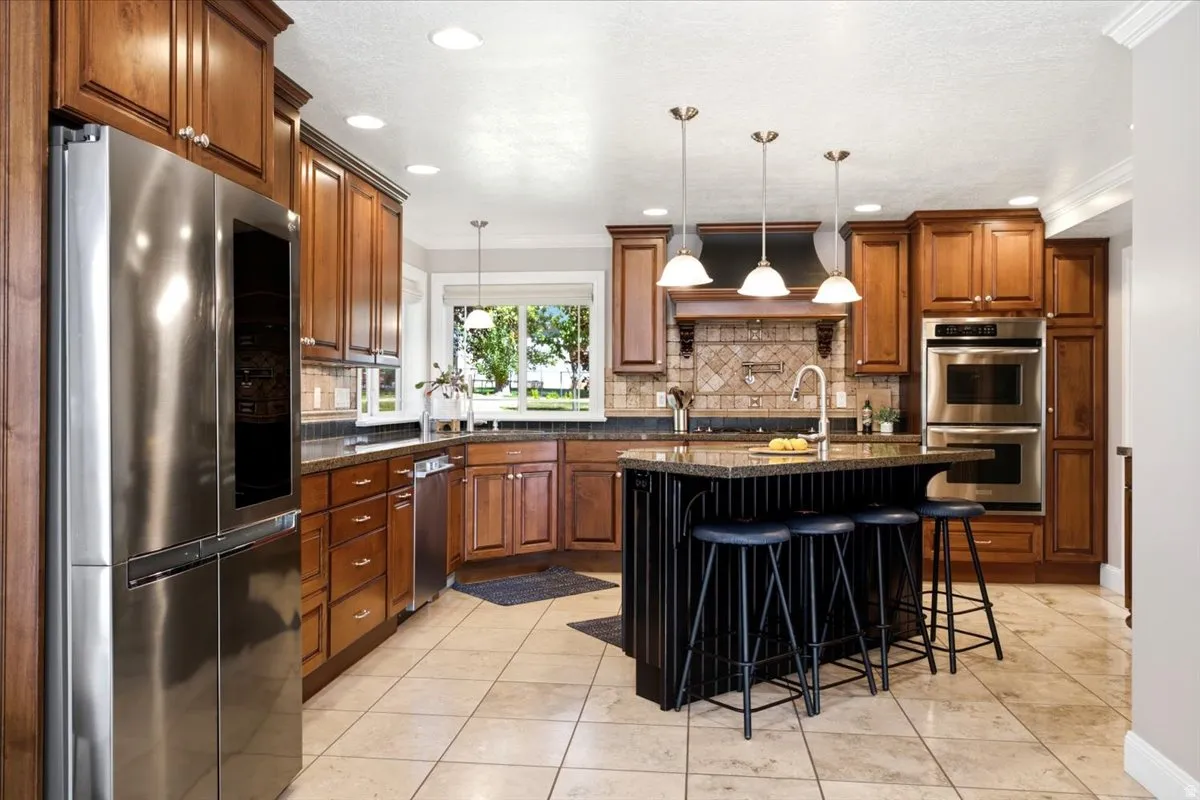 Kitchen featuring warm wood cabinetry, stainless steel appliances, a center island with pendant lighting, tile flooring, and a window above the sink