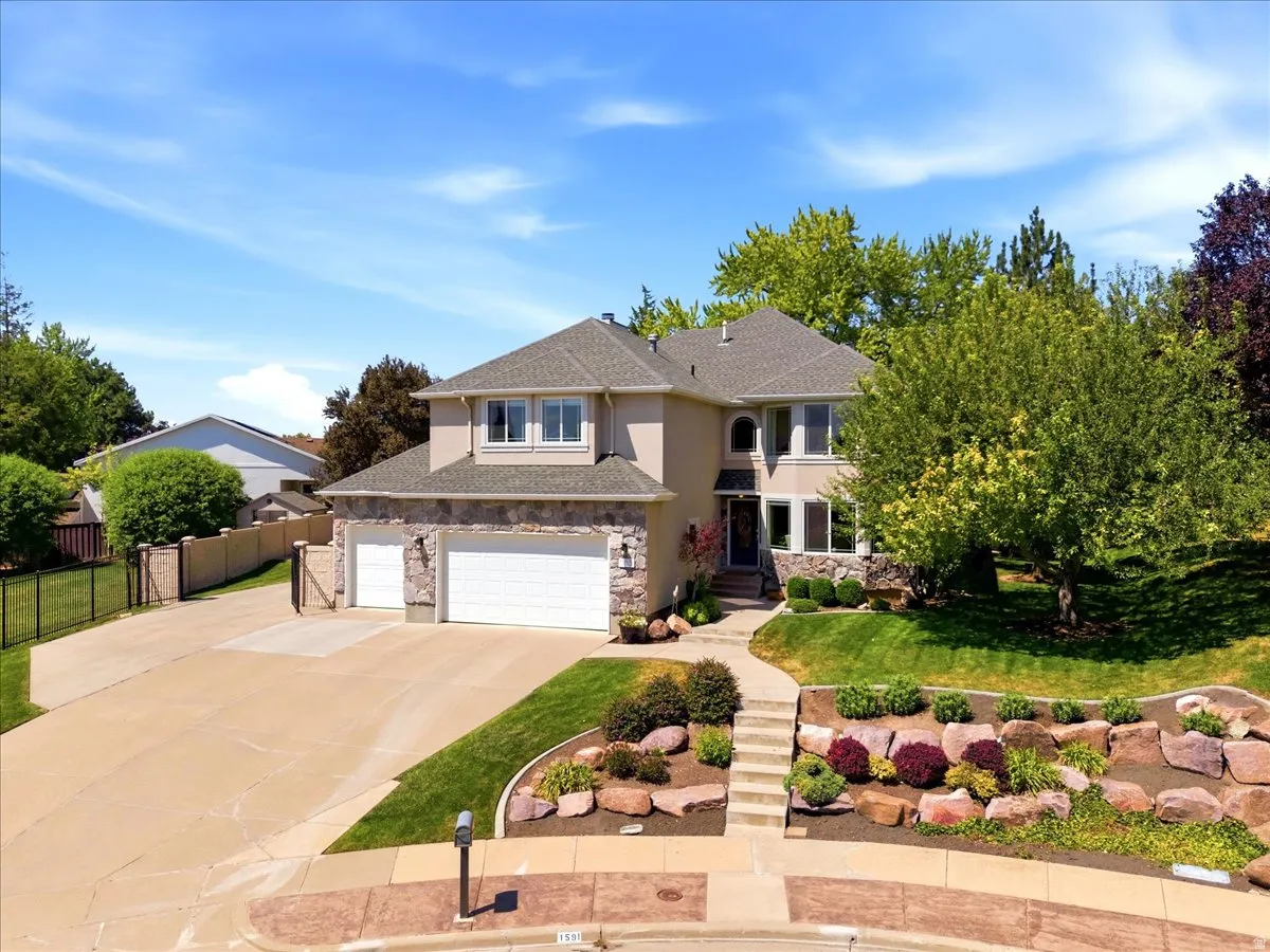 Stucco and stone exterior with a two-car garage, concrete driveway, and tiered landscaping