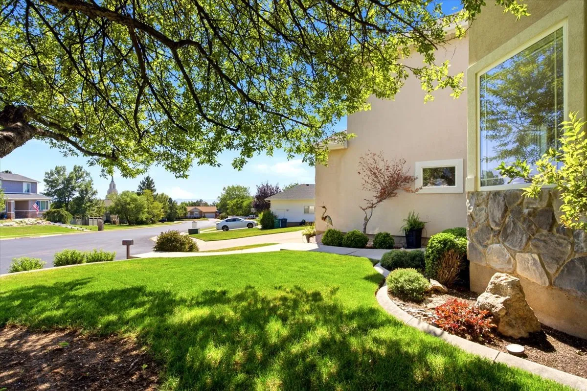 Stucco exterior with stone accents, a large picture window, and a mature tree providing shade