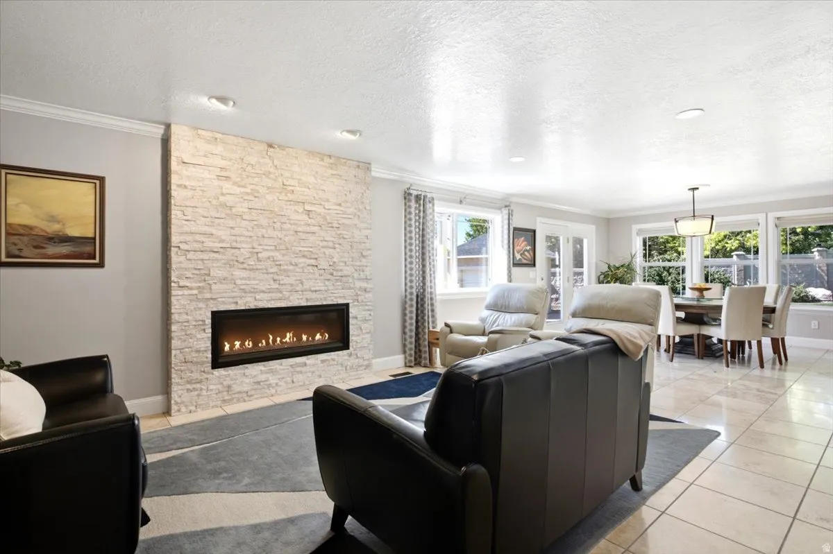 Stacked stone fireplace with a linear insert, recessed ceiling lighting, crown molding, tile flooring, and multiple windows