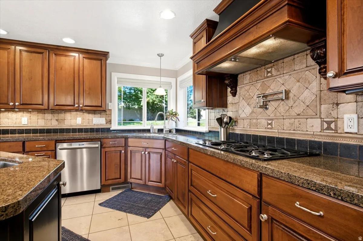 Hardwood cabinetry, granite countertops, stainless steel appliances, tiled backsplash, and tile flooring