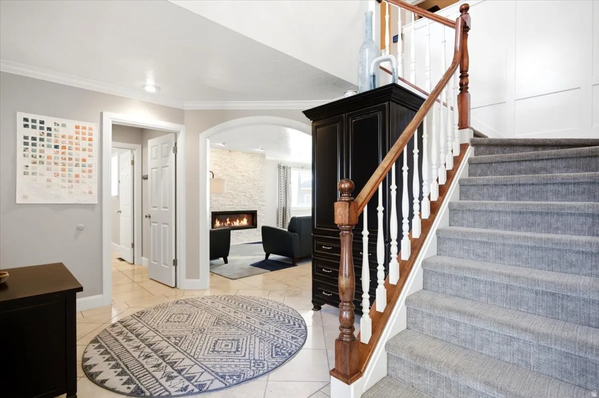 Tiled flooring, arched entry, paneling, wood and white baluster staircase, linear fireplace