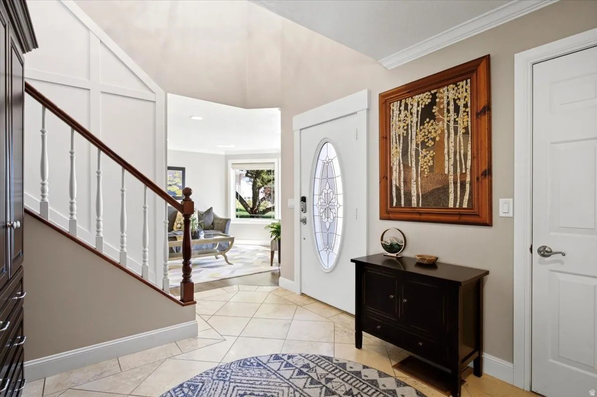 Entryway featuring a decorative oval-paneled front door, an adjacent staircase with white spindles and a wood-finish handrail, and tiled flooring