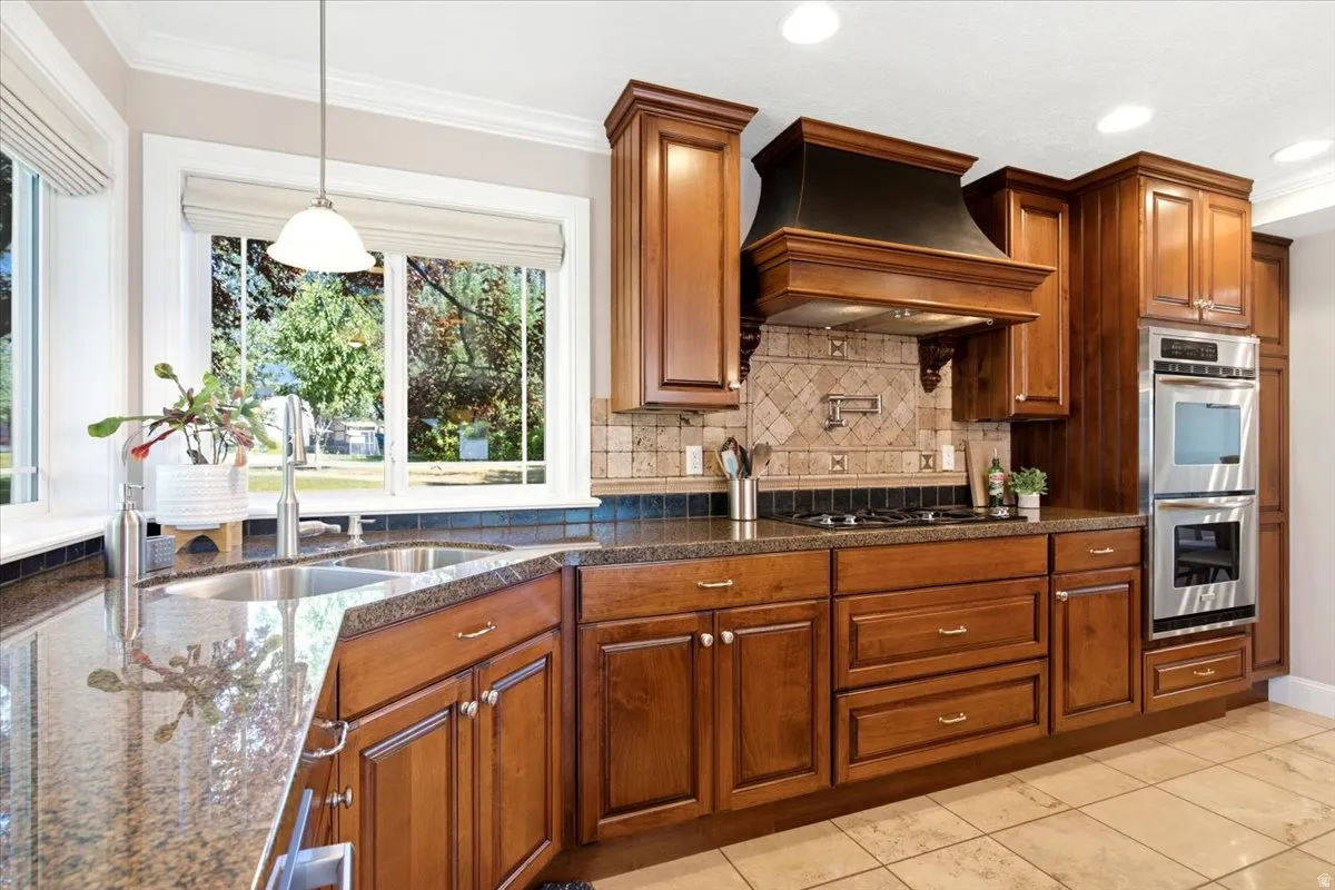Wood cabinetry with polished hardware, stainless steel double wall ovens, tile flooring, and a stone-finish backsplash