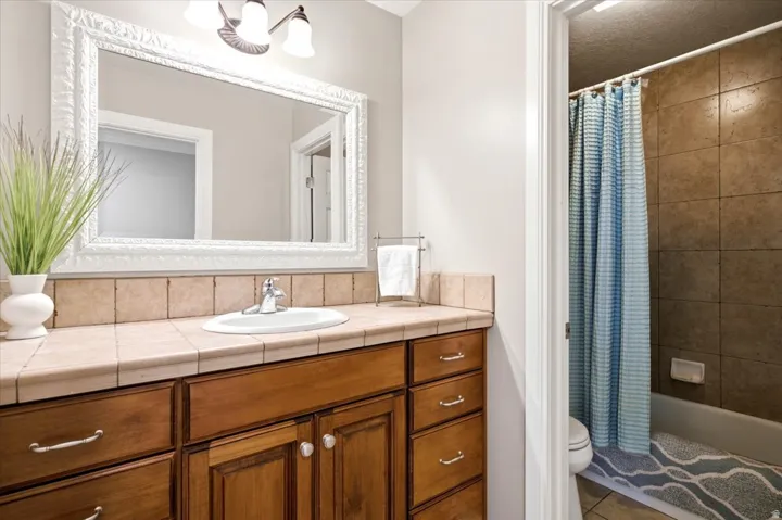 Wood-finish vanity with ample storage, ceramic tile countertop, and a large decorative framed mirror