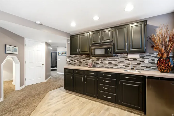 Built-in wet bar with dark cabinetry, integrated microwave, undermount sink, and stainless-steel mini-refrigerator