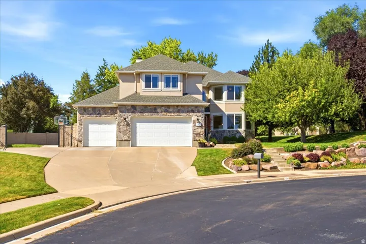 Stucco and stone exterior, two-car garage, concrete driveway, stone retaining walls, and established landscaping