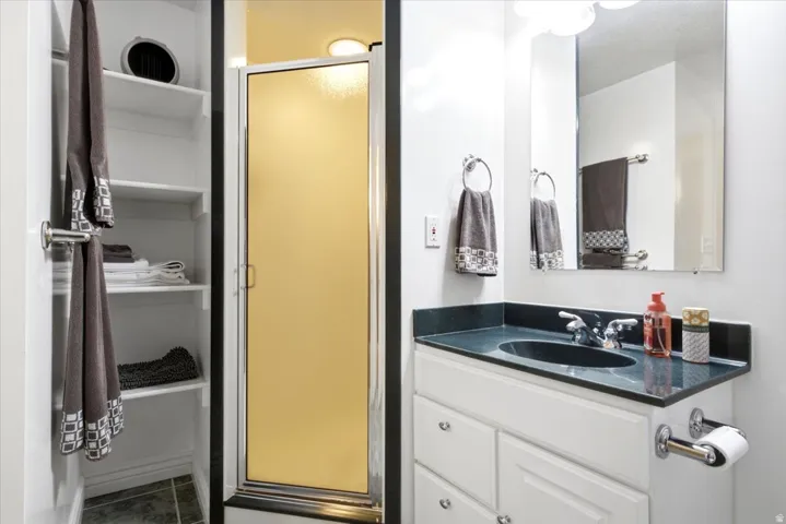 Vanity with integrated sink, chrome faucet, wall-mounted mirror, and enclosed shower