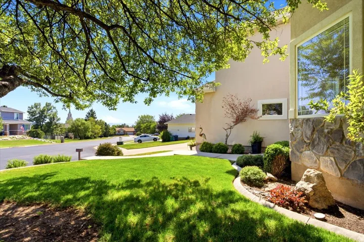 Stucco exterior with stone accents, a large picture window, and a mature tree providing shade
