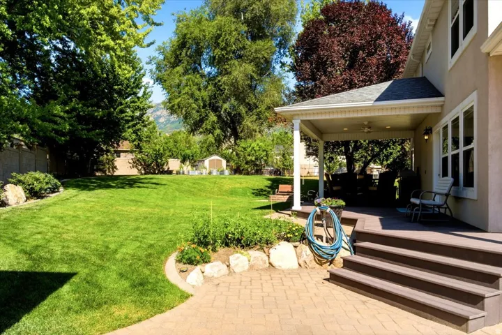 Expansive backyard featuring a large lawn, covered patio, paver patio, and composite decking with stairs