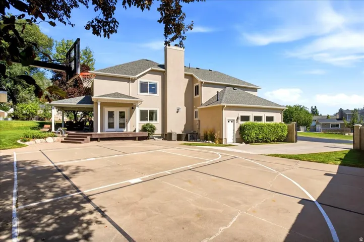 Stucco exterior with multiple windows, concrete sport court, and a covered patio featuring a built-in barbecue area