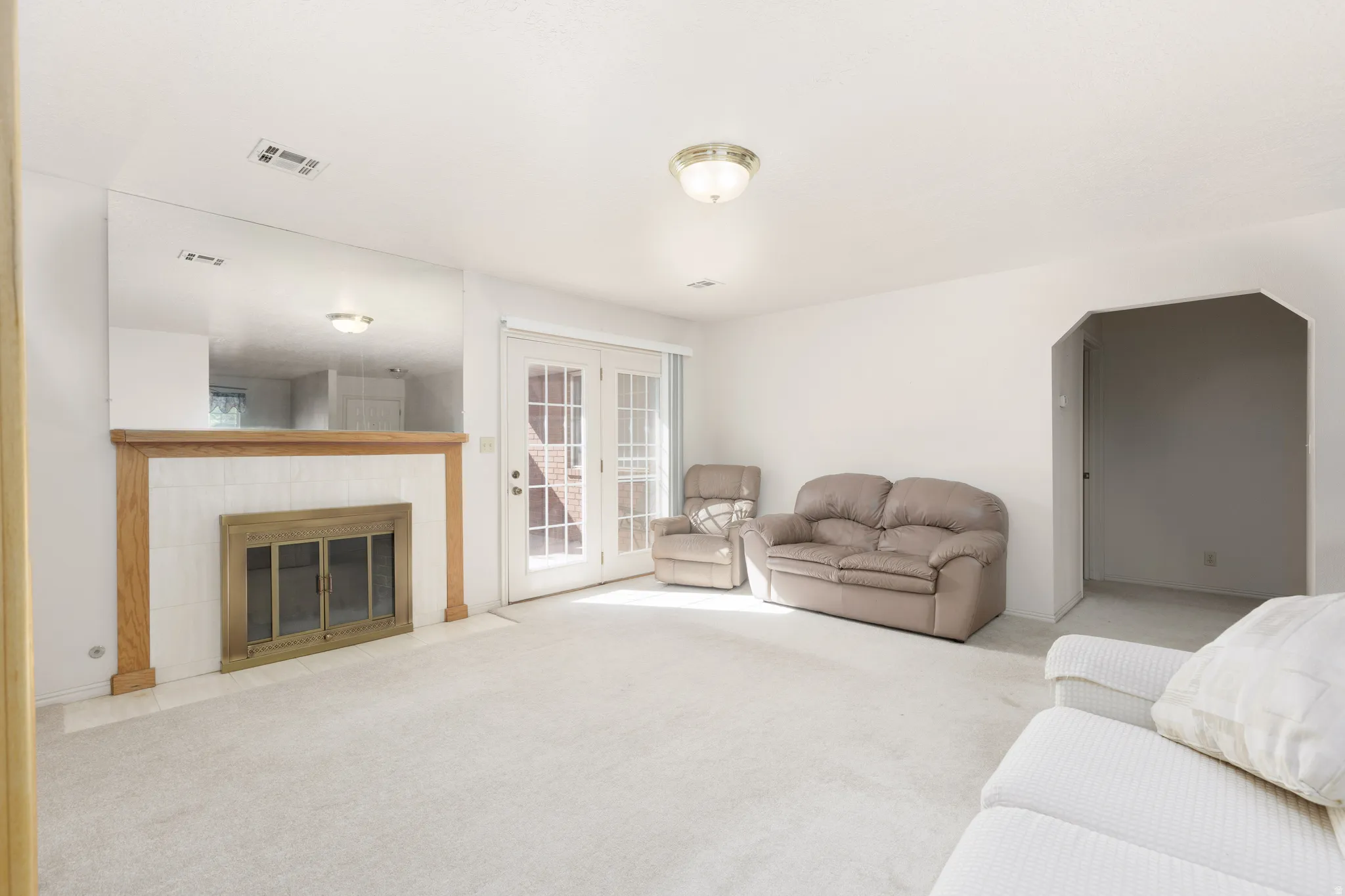 Fireplace with wood surround and tile hearth, glass-paned double doors, and an arched entry