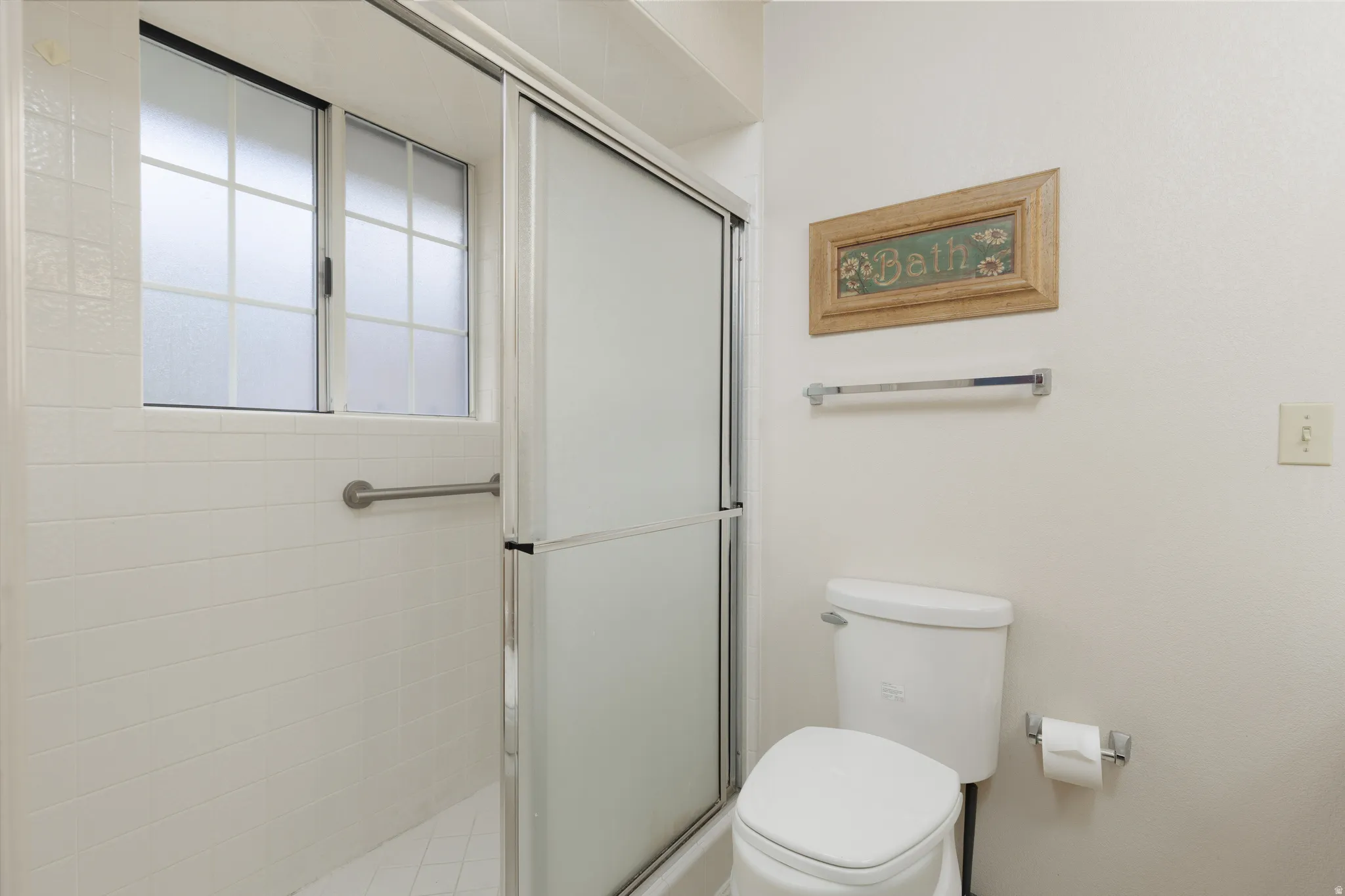 Shower enclosure with sliding frosted glass doors, white tiled walls, and a built-in grab bar