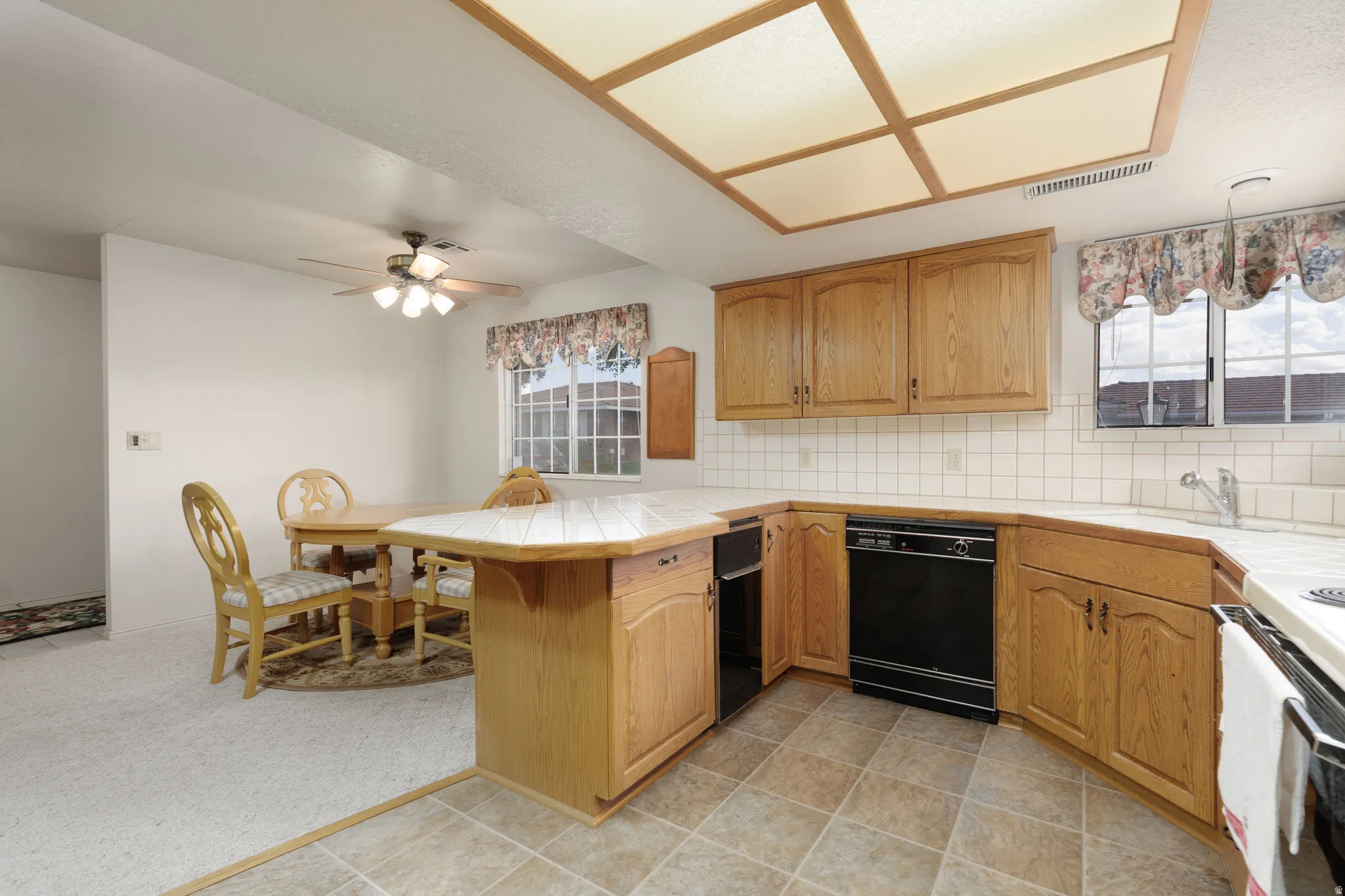 Kitchen featuring wood cabinetry, white tile countertops, and a full suite of black appliances