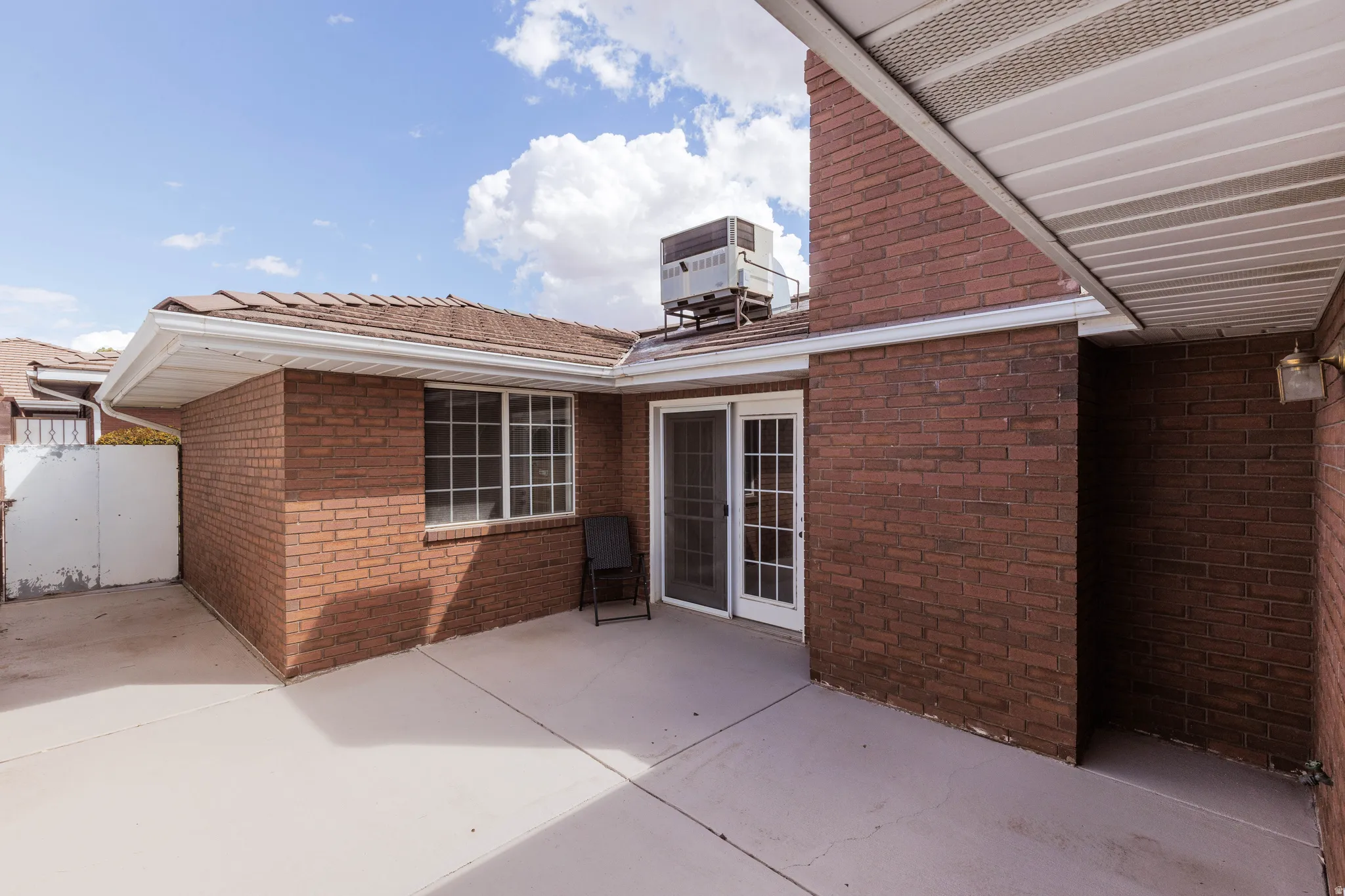 Brick exterior with a concrete patio, sliding glass door, and grid window