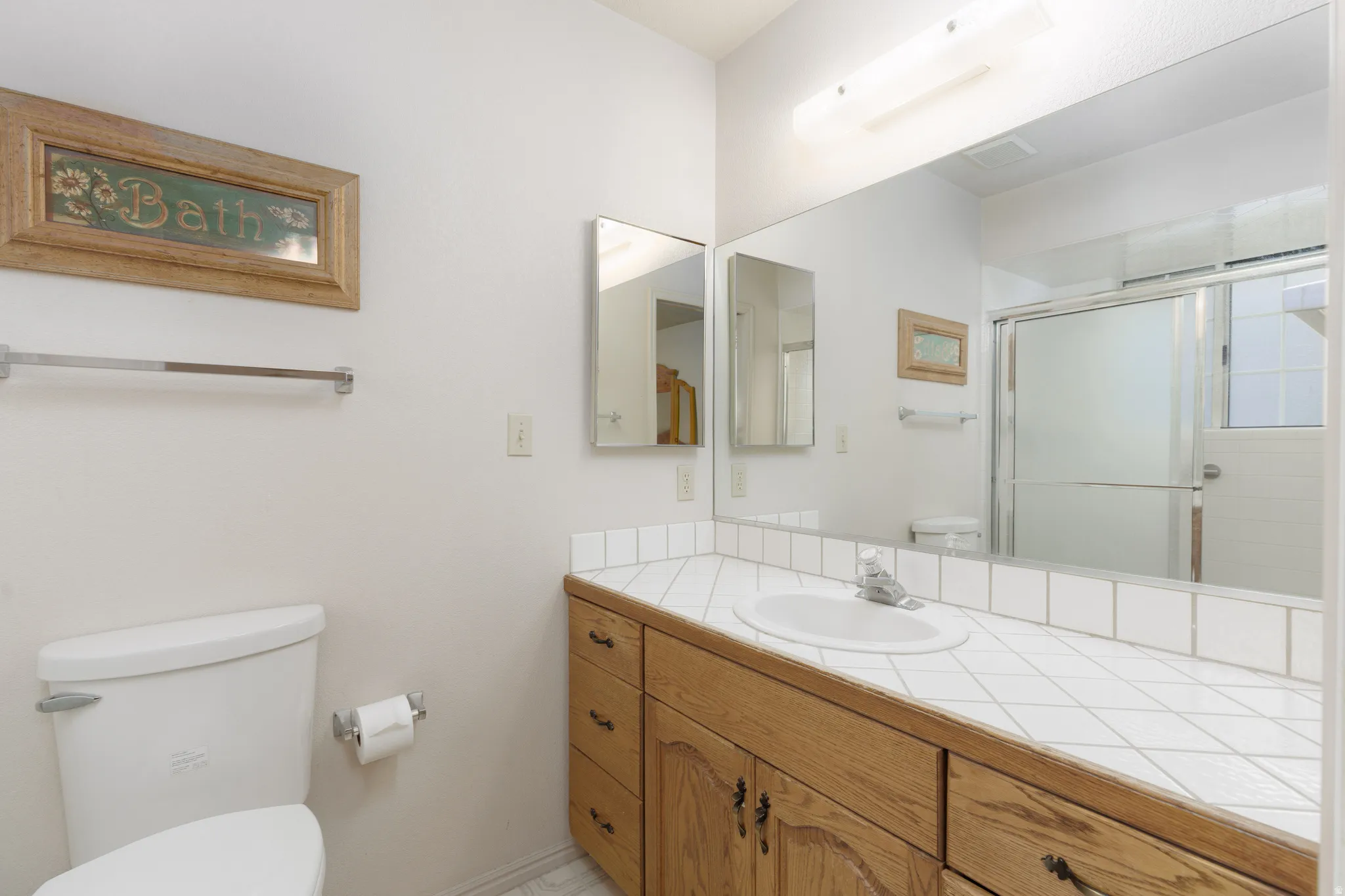 Oak wood-finish vanity with ample storage, tiled countertop, integrated sink, and large wall-mounted mirror