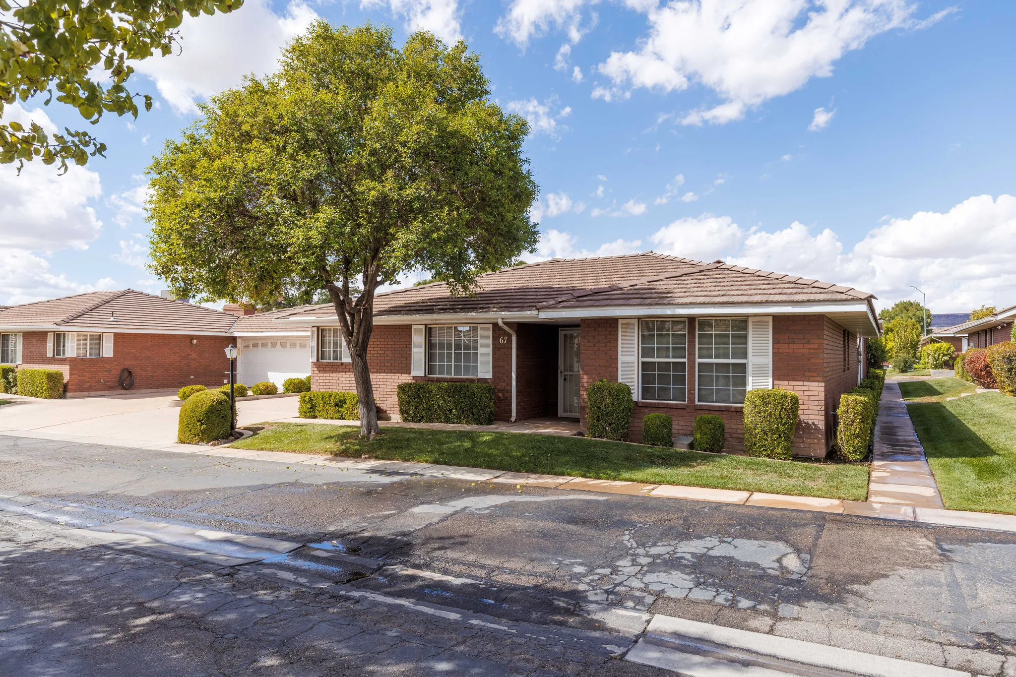 Brick exterior with white window shutters, mature tree, and manicured landscaping