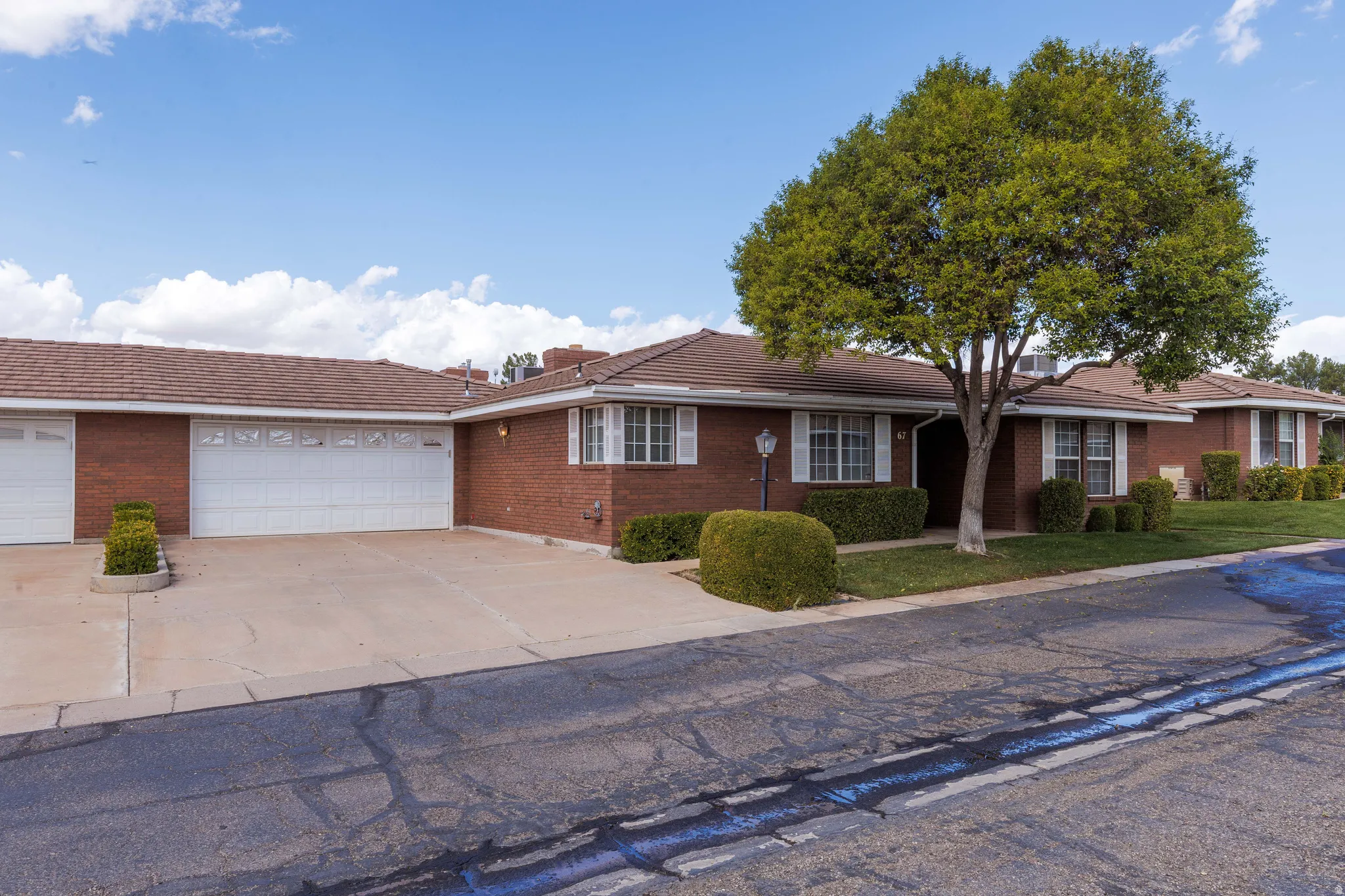 Brick exterior with white shutters, multiple garage bays, mature tree, and landscaped front yard