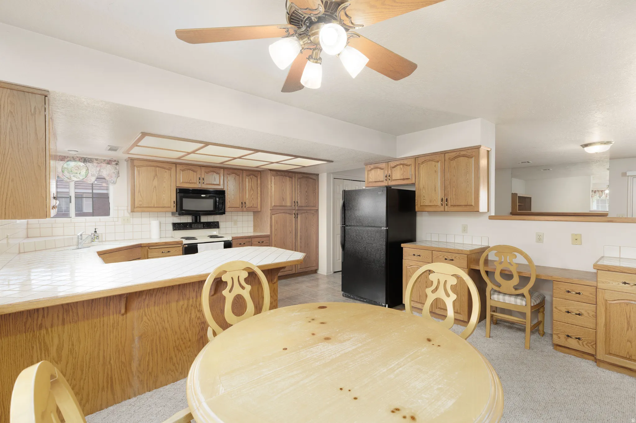 Kitchen featuring wood cabinetry, white tiled countertops, white subway tile backsplash, a black built-in microwave, and a ceiling fan