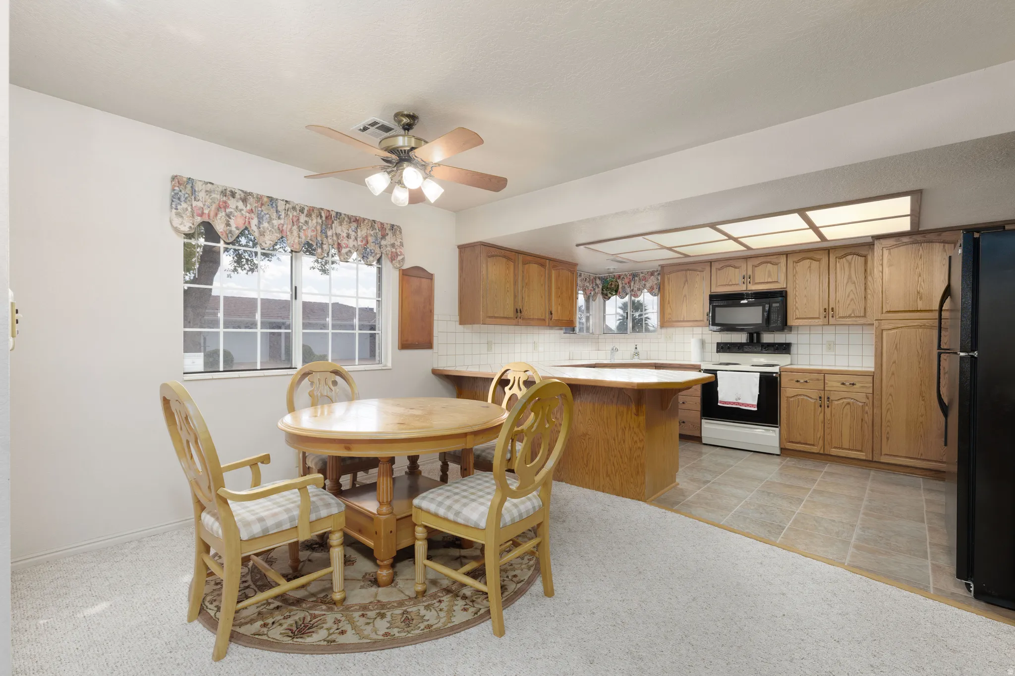 Kitchen with wood-finish cabinetry, white tile backsplash, and integrated black appliances