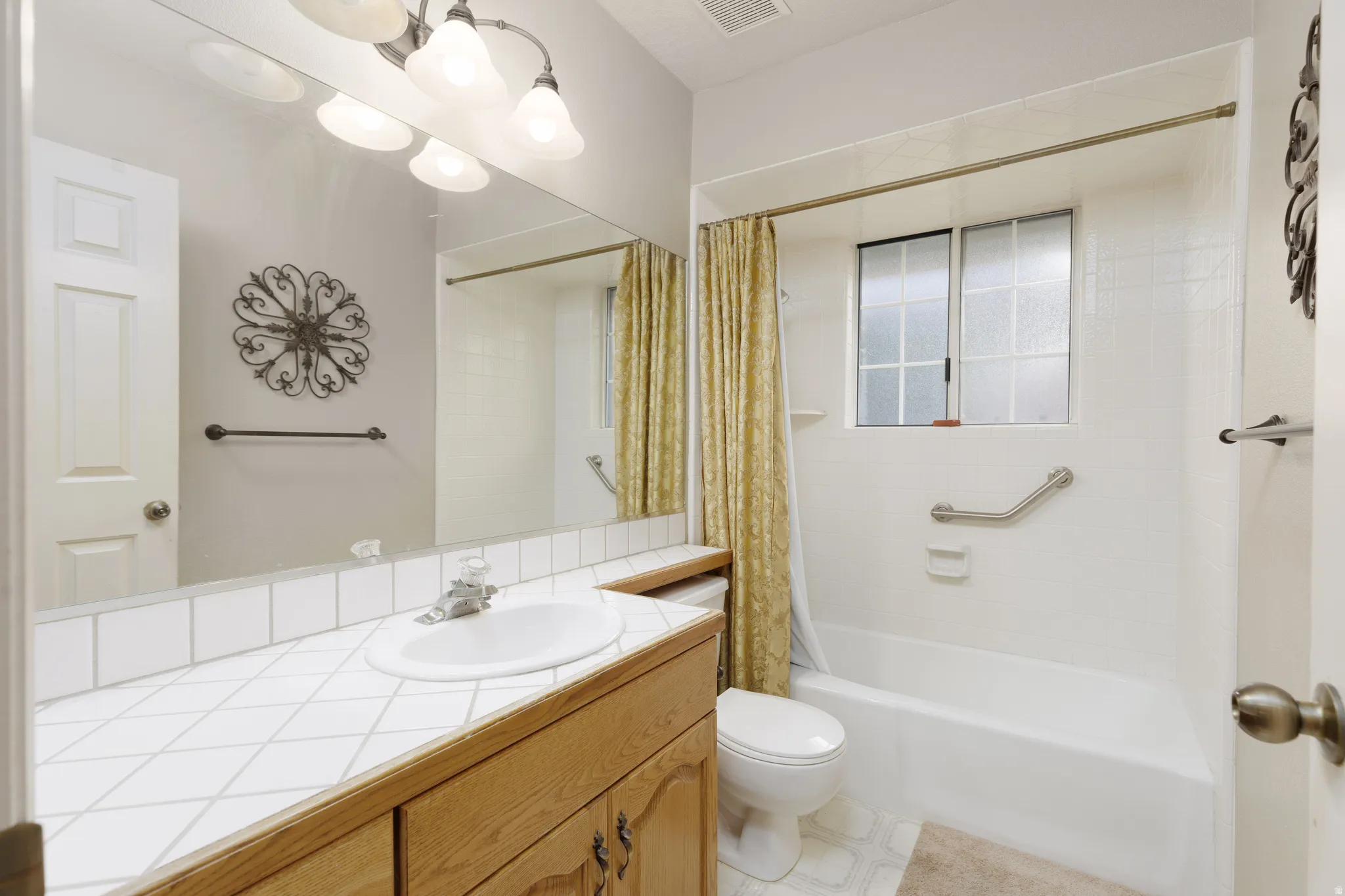 Full-width mirror over a wood-finish vanity with a tile countertop