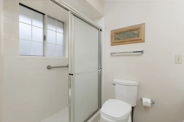 Shower enclosure with sliding frosted glass doors, white tiled walls, and a built-in grab bar