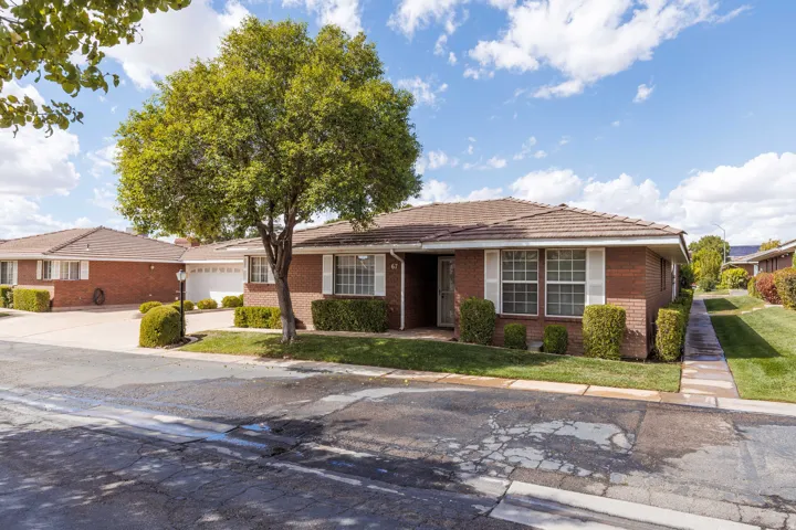 Brick exterior with white window shutters, mature tree, and manicured landscaping