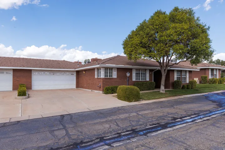 Brick exterior with white shutters, multiple garage bays, mature tree, and landscaped front yard