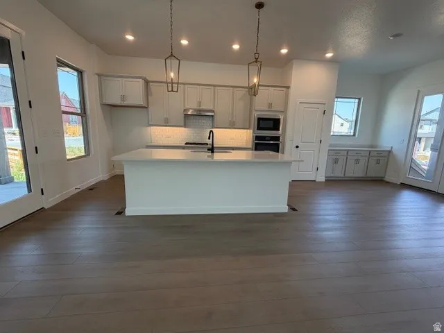 Kitchen island with a solid surface countertop, wood-finish flooring, built-in cabinetry, and pendant lighting