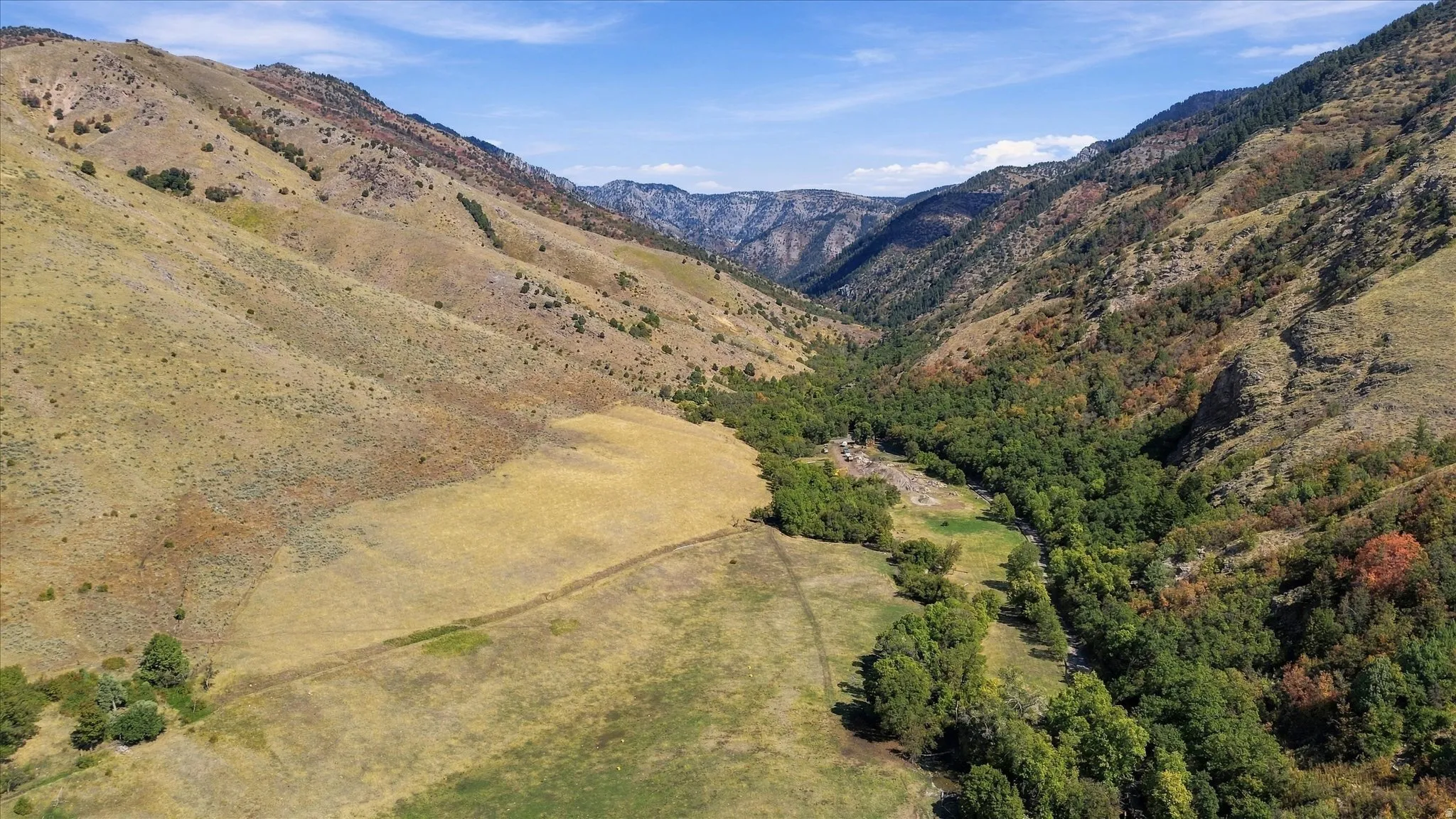 Expansive property featuring varied terrain, a valley with mature trees, and distant mountains