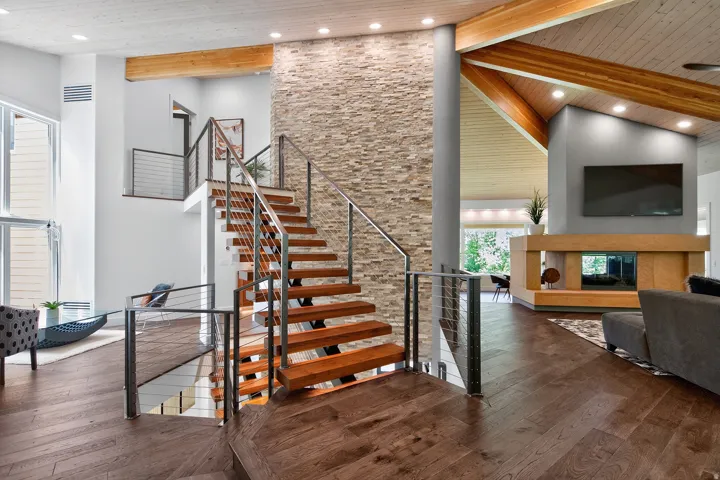Hardwood flooring throughout, a modern floating staircase with cable railings, a stone accent wall, and an open-concept living area with a fireplace