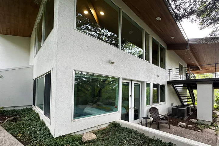 Multi-level exterior featuring white textured stucco, extensive large windows, wood-panel soffits, and a modern exterior staircase with railing