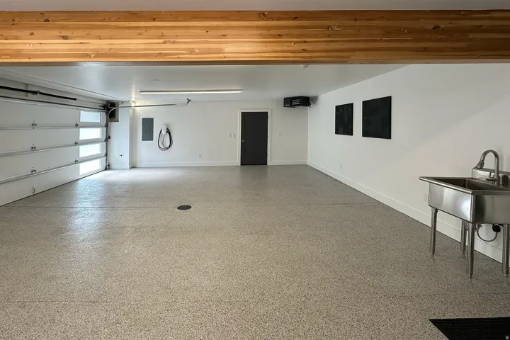 Spacious garage with an epoxy floor finish, exposed wood beam, modern garage door with translucent panels, and a utility sink