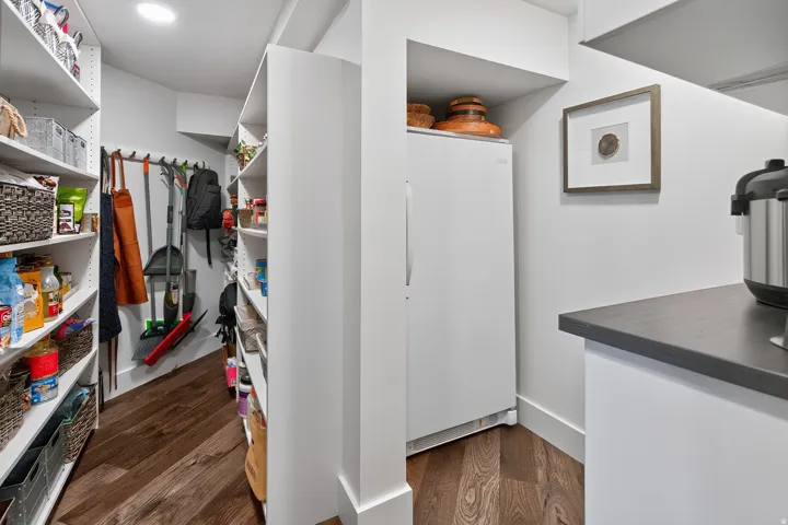 Walk-in pantry with extensive built-in shelving, wood-finish flooring, and recessed ceiling lighting