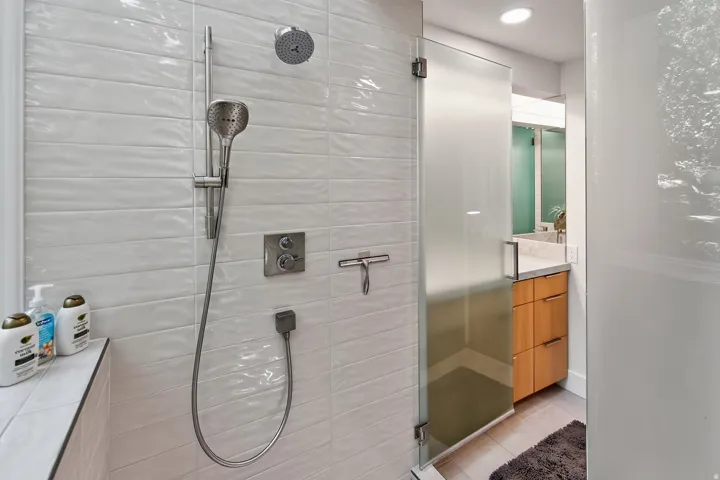 Shower with white textured tile, dual shower heads, and an adjacent frosted glass enclosure