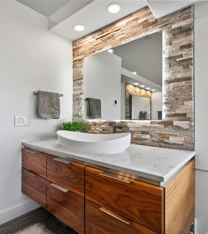 Floating wood-finish vanity with six drawers, a vessel sink, and a stone-tiled mirror surround with integrated lighting