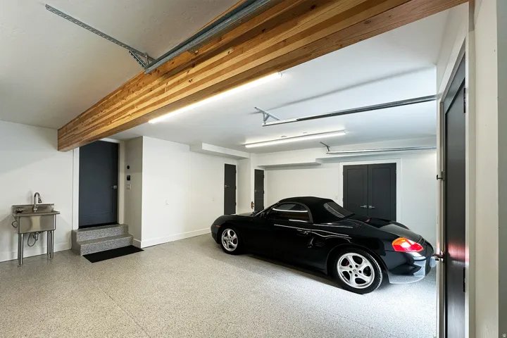 Spacious garage with an epoxy flooring, exposed wood beam, multiple doors, and a utility sink