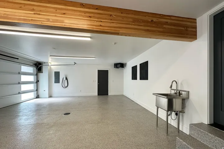 Attached garage with wood-finish beam, light-colored floor coating, and a utility sink