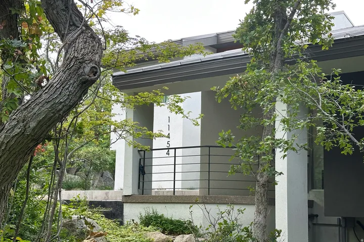Exterior with horizontal railing, exposed aggregate foundation, and mature trees