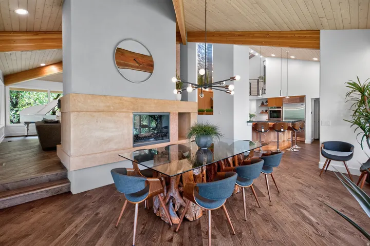 Vaulted wood-paneled ceilings, exposed wood beams, a stone-clad fireplace with a glass enclosure, wood-finish flooring, and a modern chandelier