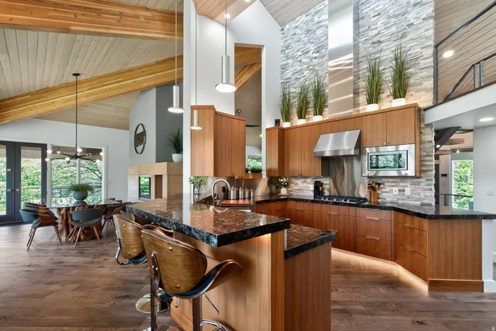 Vaulted wood-paneled ceiling with exposed beams, wood-finish flooring, kitchen island with dark stone countertop, stainless steel appliances, and a stacked stone accent wall