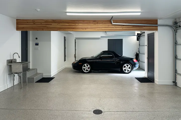 Two-car garage featuring an epoxy-coated concrete floor, stainless steel utility sink, and wood-finish ceiling beam