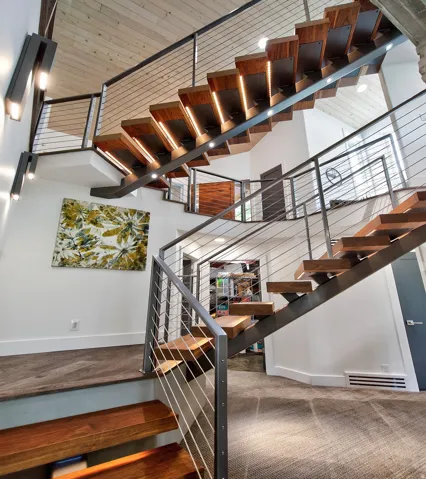 Floating wood-finish stairs with integrated lighting, cable railing, and a wood-paneled ceiling