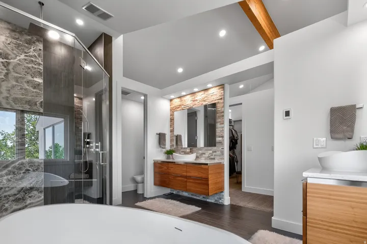 Freestanding soaking tub, glass-enclosed shower with stone-finish walls, dual floating vanities, and wood-finish flooring
